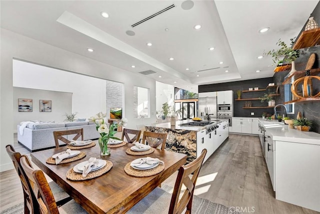 dining area featuring a raised ceiling, sink, and light wood-type flooring