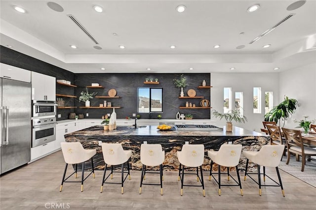 kitchen featuring a large island with sink, a kitchen breakfast bar, white cabinets, and built in refrigerator