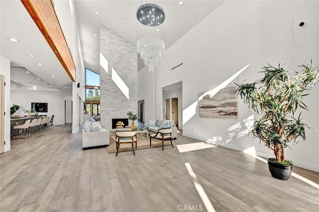 living room with a notable chandelier, a towering ceiling, a stone fireplace, and light hardwood / wood-style floors