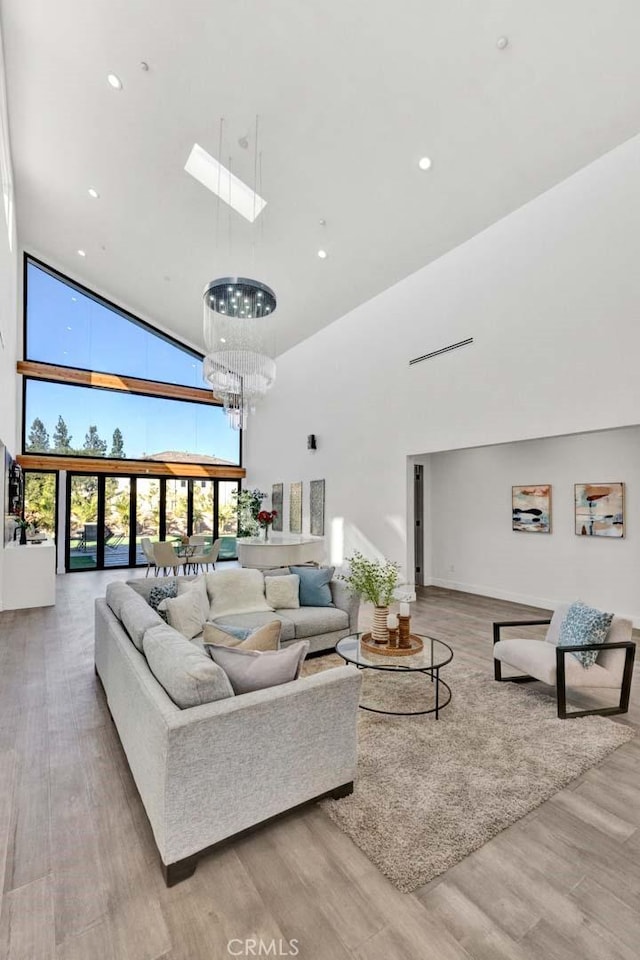 living room featuring light hardwood / wood-style floors, a chandelier, high vaulted ceiling, and a skylight