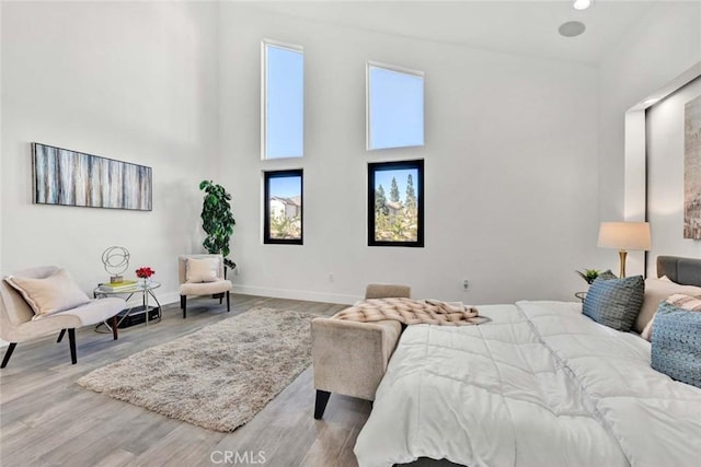 bedroom with multiple windows, a towering ceiling, and light hardwood / wood-style flooring