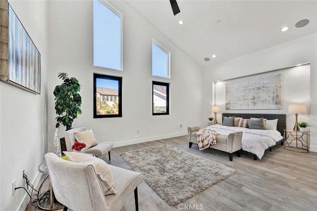 bedroom with ceiling fan, light wood-type flooring, and a high ceiling