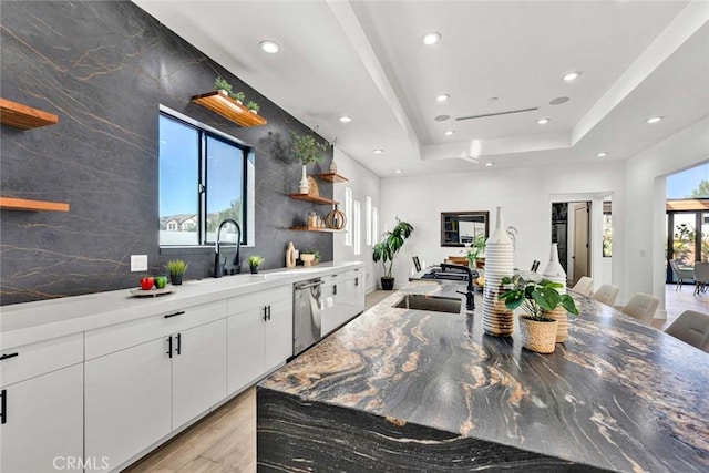 kitchen with sink, white cabinetry, light wood-type flooring, dishwasher, and a raised ceiling