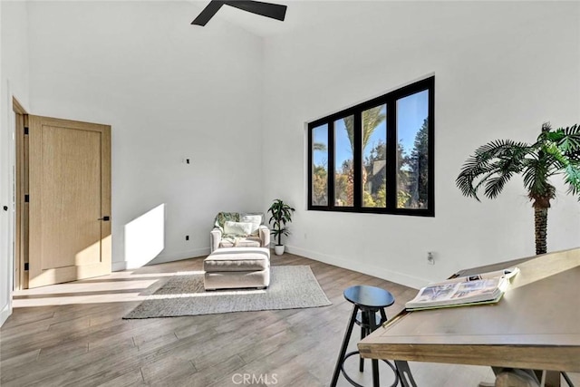 living area featuring hardwood / wood-style flooring, ceiling fan, and a high ceiling