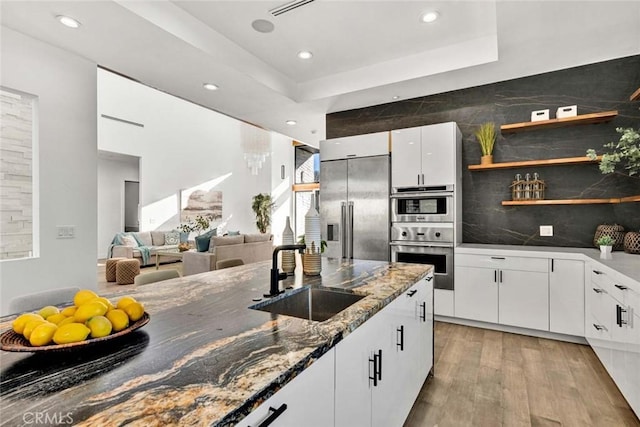 kitchen with sink, stainless steel appliances, a tray ceiling, white cabinets, and dark stone counters