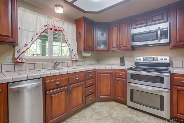 kitchen with appliances with stainless steel finishes, sink, tile countertops, and light tile patterned floors