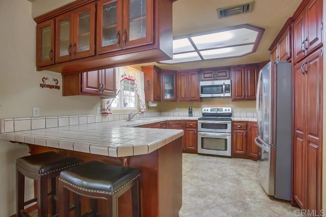 kitchen with sink, a breakfast bar area, tile countertops, kitchen peninsula, and stainless steel appliances