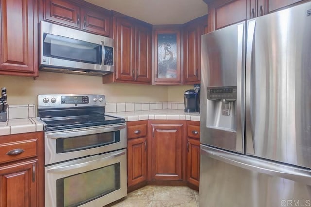 kitchen with appliances with stainless steel finishes, tile counters, and light tile patterned floors