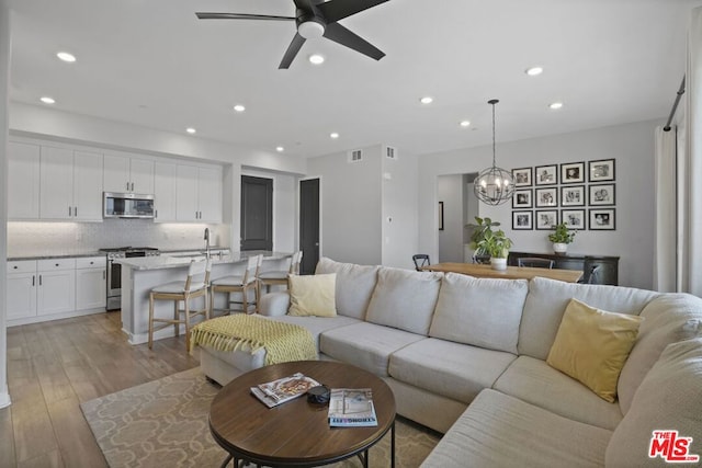 living room with ceiling fan with notable chandelier and light hardwood / wood-style floors