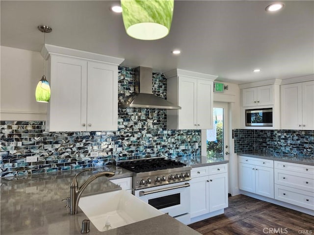 kitchen with wall chimney range hood, white cabinetry, stainless steel microwave, gas range oven, and decorative light fixtures