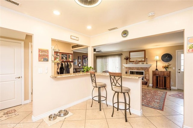 kitchen with crown molding, a breakfast bar, a fireplace, light tile patterned flooring, and kitchen peninsula