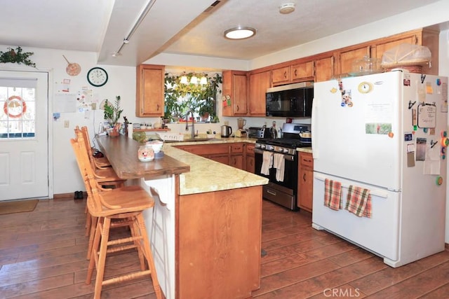 kitchen with dark hardwood / wood-style floors, stainless steel range with gas stovetop, kitchen peninsula, and white refrigerator