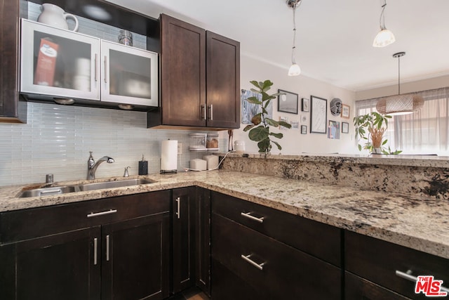 kitchen featuring dark brown cabinetry, sink, light stone counters, tasteful backsplash, and pendant lighting