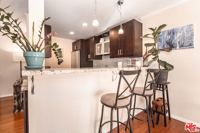 kitchen featuring dark brown cabinetry, high quality fridge, backsplash, and a breakfast bar