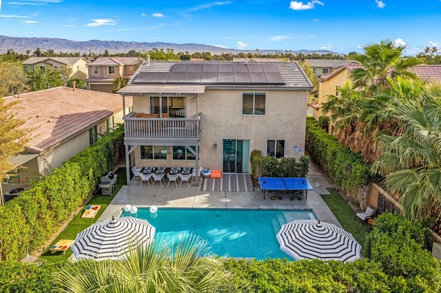 back of property with a patio, a balcony, a mountain view, and solar panels