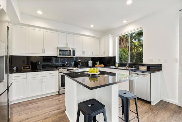 kitchen with appliances with stainless steel finishes, white cabinetry, a kitchen breakfast bar, tasteful backsplash, and light wood-type flooring