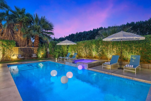 pool at dusk featuring an in ground hot tub and a patio