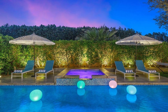 pool at dusk featuring an in ground hot tub and a patio