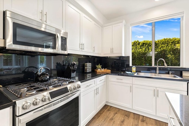 kitchen featuring sink, white cabinets, decorative backsplash, stainless steel appliances, and light hardwood / wood-style flooring