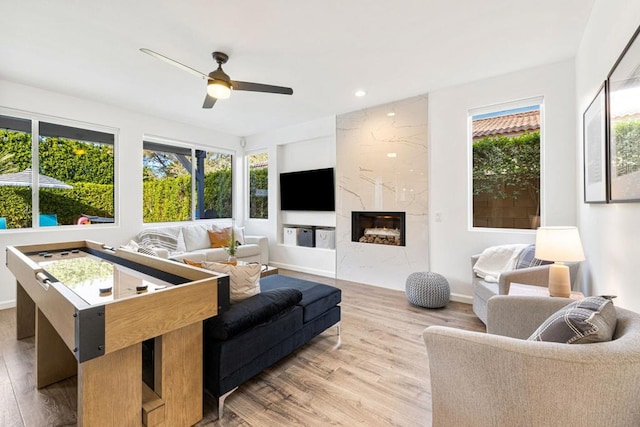 living room featuring ceiling fan, plenty of natural light, light wood-type flooring, and a high end fireplace