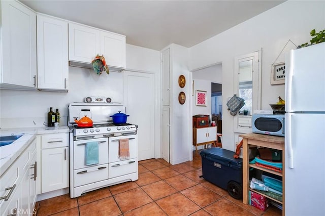 kitchen with light tile patterned floors, white appliances, light stone countertops, and white cabinets