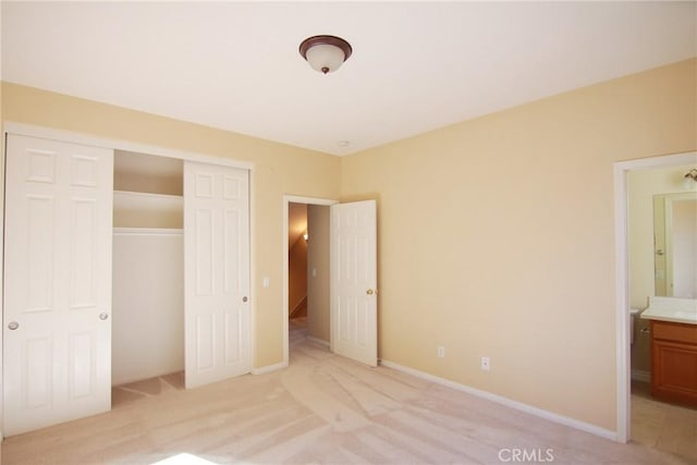 unfurnished bedroom with ensuite bath, a closet, and light carpet