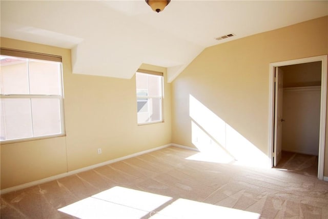 unfurnished bedroom featuring a walk in closet, lofted ceiling, a closet, and light carpet