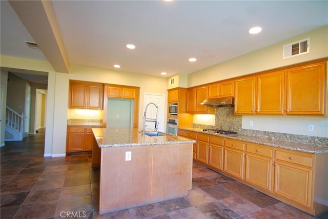 kitchen featuring sink, stainless steel appliances, light stone countertops, a kitchen island with sink, and decorative backsplash