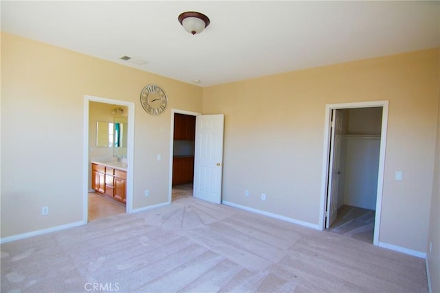 unfurnished bedroom featuring a closet, ensuite bathroom, a spacious closet, and light carpet