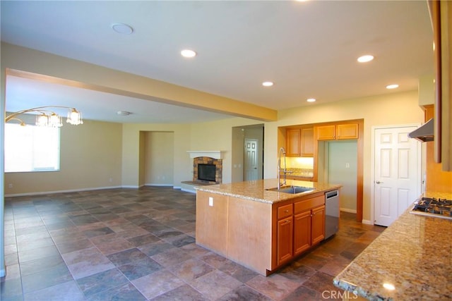 kitchen with sink, a center island with sink, stainless steel appliances, a fireplace, and light stone countertops