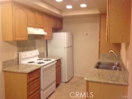 kitchen featuring light stone counters, sink, white appliances, and a raised ceiling