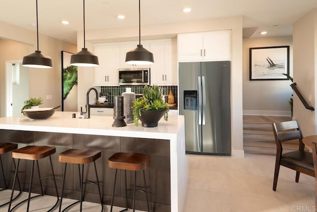 kitchen featuring white cabinetry, hanging light fixtures, stainless steel appliances, a kitchen breakfast bar, and decorative backsplash