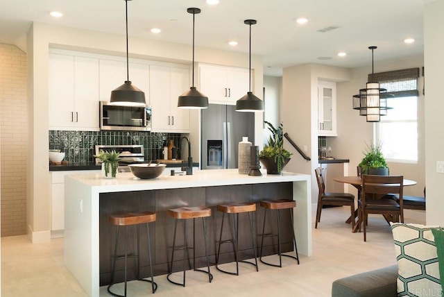 kitchen with appliances with stainless steel finishes, a kitchen island with sink, pendant lighting, and white cabinets