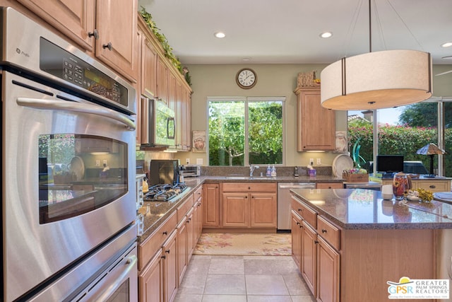 kitchen with light brown cabinetry, decorative light fixtures, light tile patterned floors, appliances with stainless steel finishes, and dark stone counters