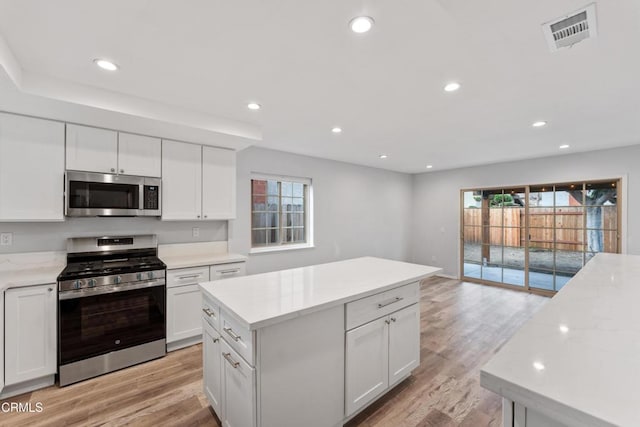 kitchen with appliances with stainless steel finishes, a wealth of natural light, a kitchen island, and white cabinets