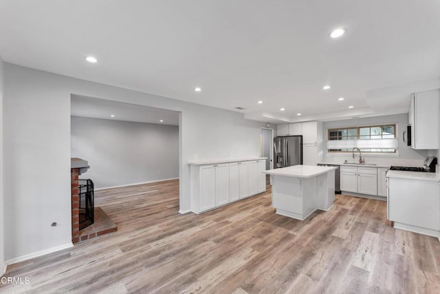 kitchen with white cabinets, a center island, light hardwood / wood-style floors, stainless steel appliances, and a brick fireplace