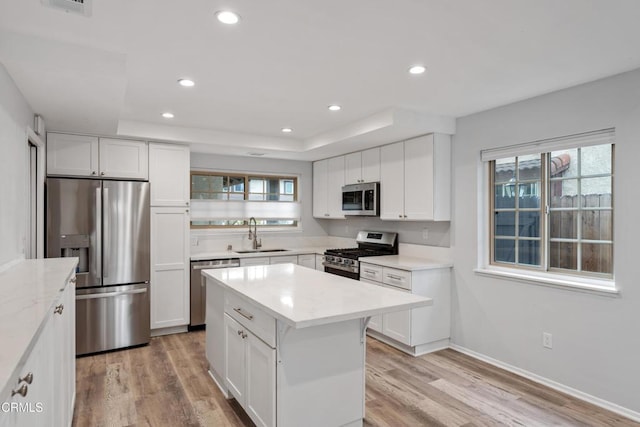 kitchen featuring a kitchen island, appliances with stainless steel finishes, white cabinetry, sink, and light hardwood / wood-style flooring