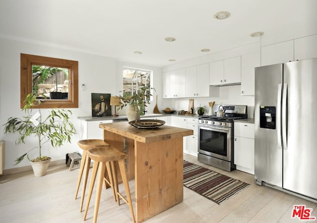 kitchen featuring white cabinetry, light hardwood / wood-style flooring, ornamental molding, and appliances with stainless steel finishes