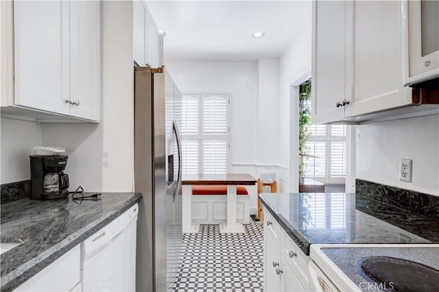 kitchen featuring dark stone countertops, stainless steel fridge, dishwasher, and white cabinets