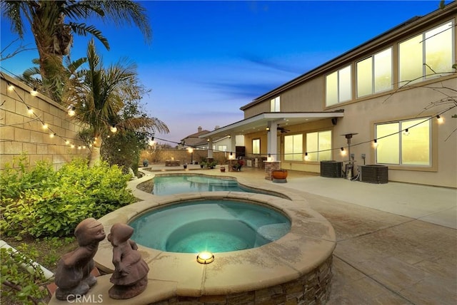 pool at dusk with an in ground hot tub, cooling unit, and a patio