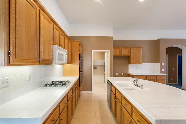 kitchen with sink, backsplash, a kitchen island with sink, tile counters, and stainless steel appliances