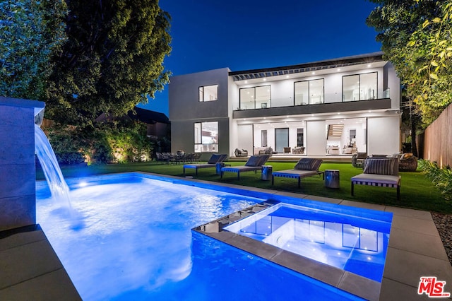 back house at twilight featuring a swimming pool with hot tub, a patio, and a lawn