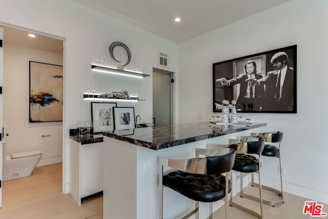 bar with dark stone countertops, light hardwood / wood-style flooring, and white cabinets