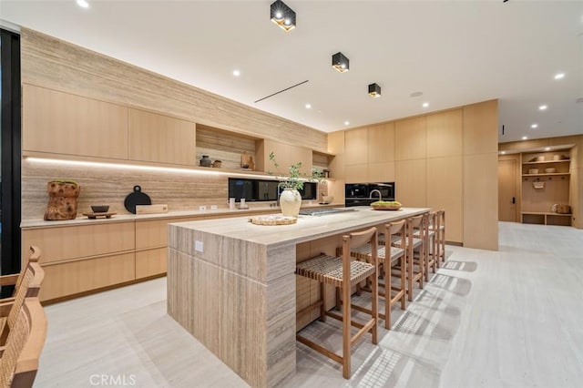 kitchen with an island with sink, a breakfast bar area, and light brown cabinets