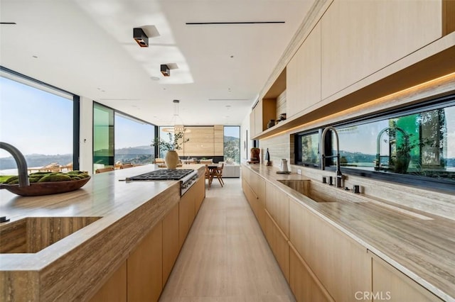 kitchen featuring sink, light brown cabinetry, decorative light fixtures, stainless steel gas stovetop, and light wood-type flooring