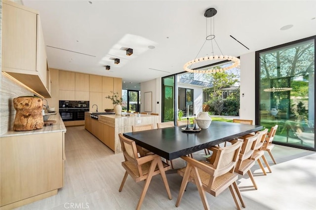 kitchen featuring tasteful backsplash, expansive windows, hanging light fixtures, light brown cabinets, and light hardwood / wood-style flooring