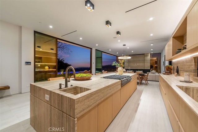 kitchen featuring a spacious island, light brown cabinetry, sink, hanging light fixtures, and stainless steel gas stovetop