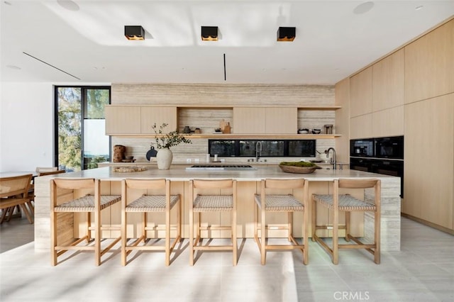 kitchen featuring a center island with sink, light brown cabinetry, and a wall of windows