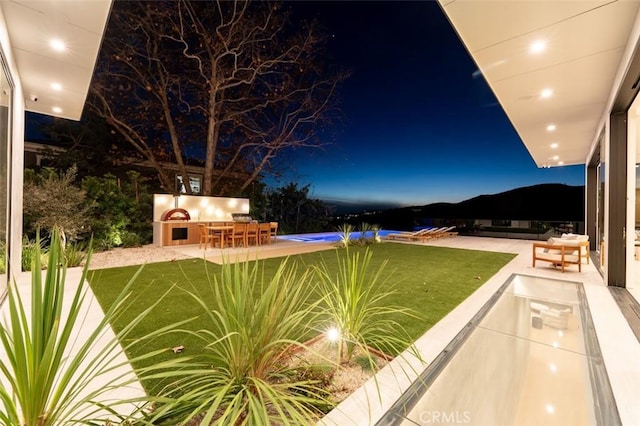 pool at twilight with a bar, a mountain view, a yard, and a patio