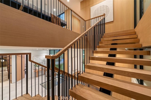 staircase featuring a towering ceiling and wooden walls